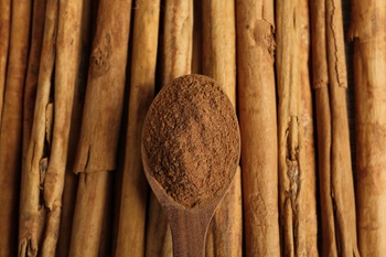 Wooden spoon with aromatic cinnamon powder over sticks, top view.